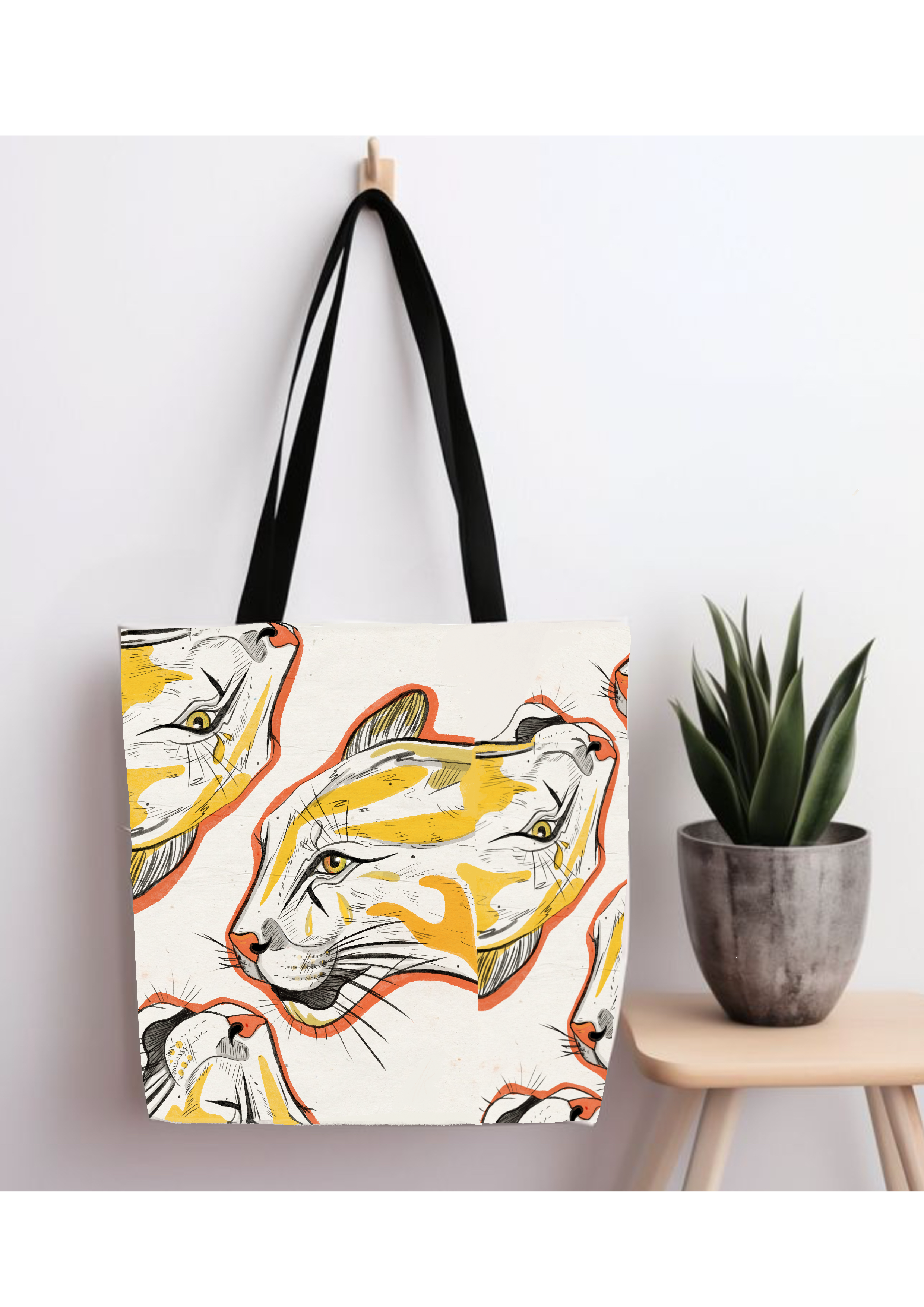 Sac de style minimaliste avec une illustration graphique de félins aux traits expressifs et couleurs jaune et orange, suspendu dans un intérieur moderne, accompagné d’une plante décorative.